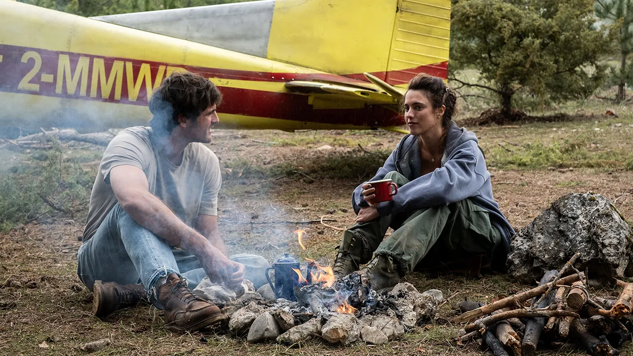 Jacob Elordi and Margaret Qualley sit together beside a campfire near a small aircraft in The Dog Stars.
