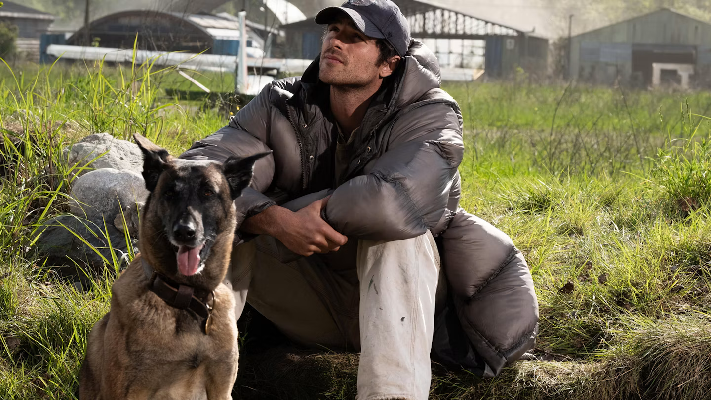 Jacob Elordi sits in the grass beside Jasper in The Dog Stars.
