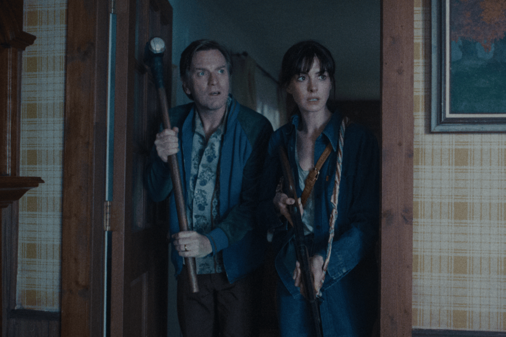 Ewan McGregor and Anne Hathaway stand armed in a doorway in The End of Oak Street.