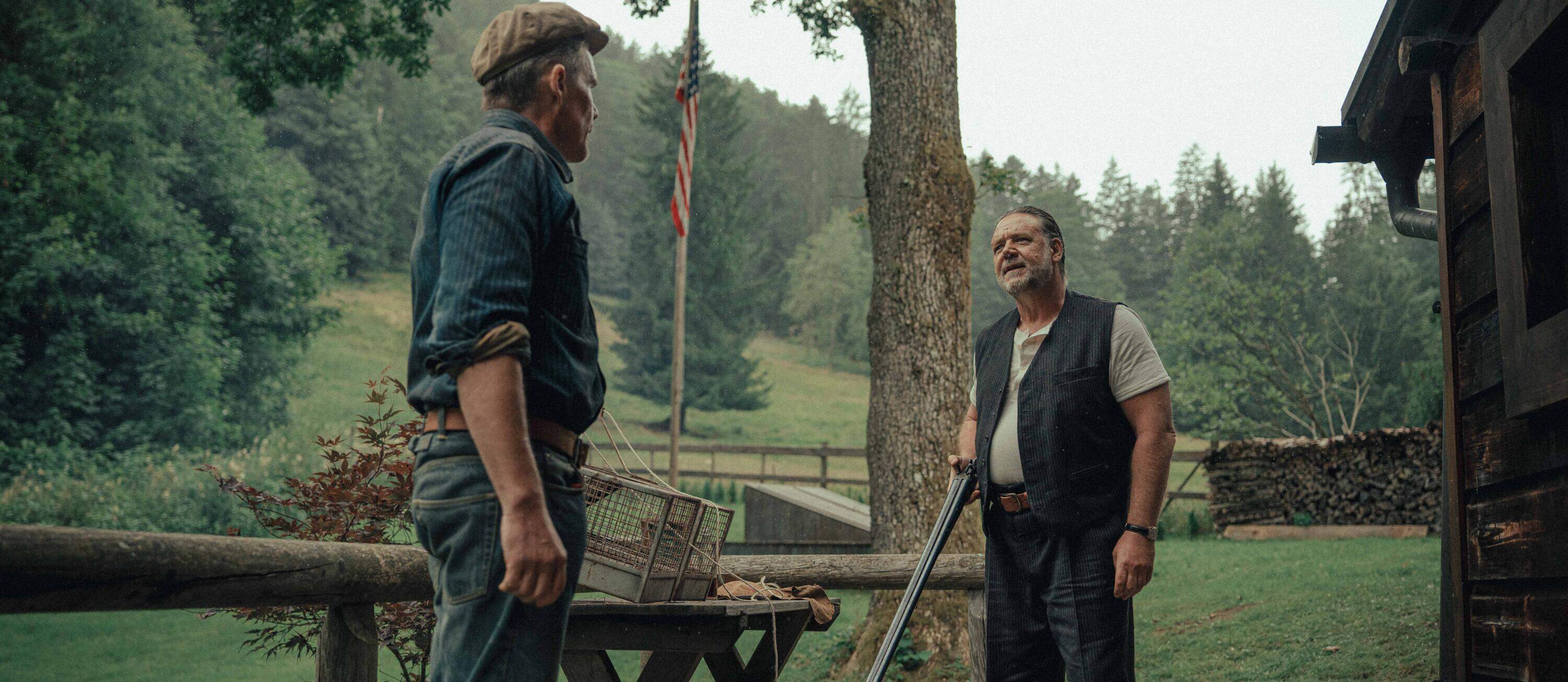 Ethan Hawke faces Russell Crowe, who holds a shotgun outside a rustic work camp in the rain.