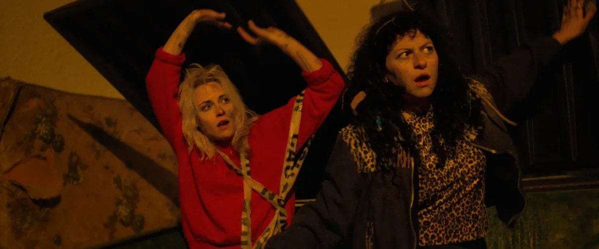 Kristen Stewart and Alia Shawkat react in surprise inside a dimly lit room in The Wrong Girls.